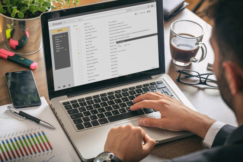 Man working with a laptop. Emails list on the screen, office background